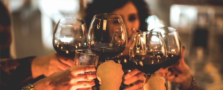 A group of people raise wine glasses brought up in a cheers.