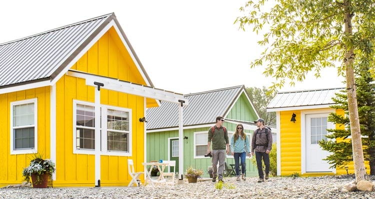 A group of three young adults ready for adventure walk among a group of colorful tiny homes