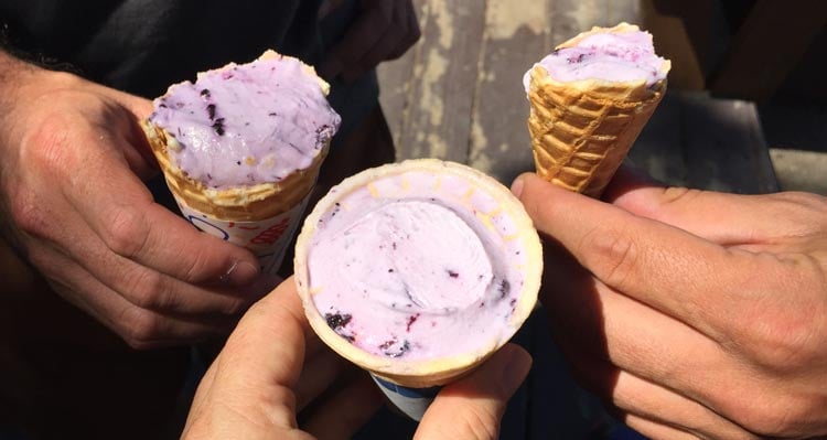 Three cones of purple ice cream held together by three people