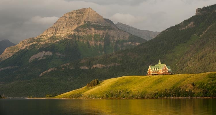 The Prince of Wales Hotel stands on a hill above a lake with mountains behind.