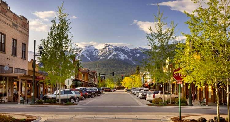 A view down Central Ave in Whitefish, MT. A tree-lined street with a view towards a snow-capped mountain.