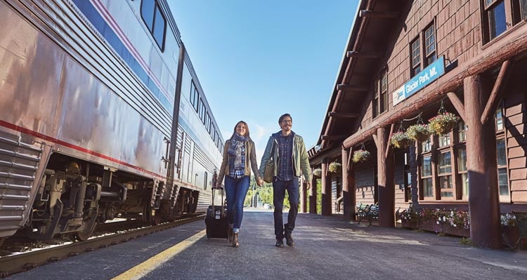 Two people walk between a train and the Amtrak train station.