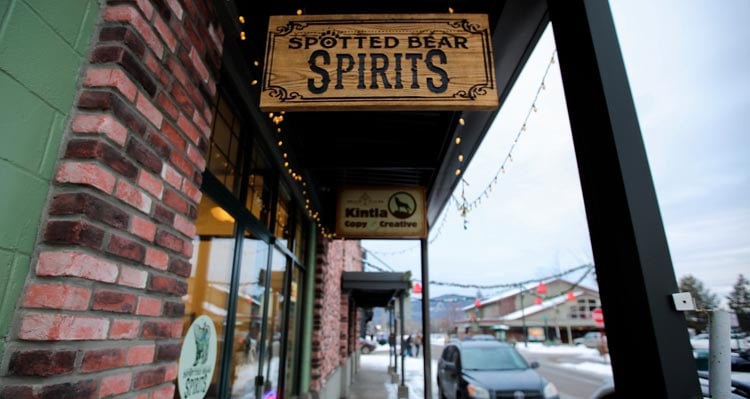 A hanging wooden sign for Spotted Bear Spirits above the sidewalk in downtown Whitefish.