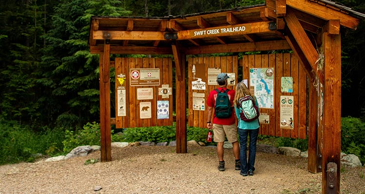 Two people look at a trailhead information board.