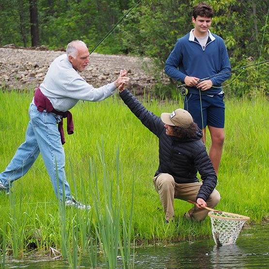 A fishing instructor high fives a a student holding a fish in a net.