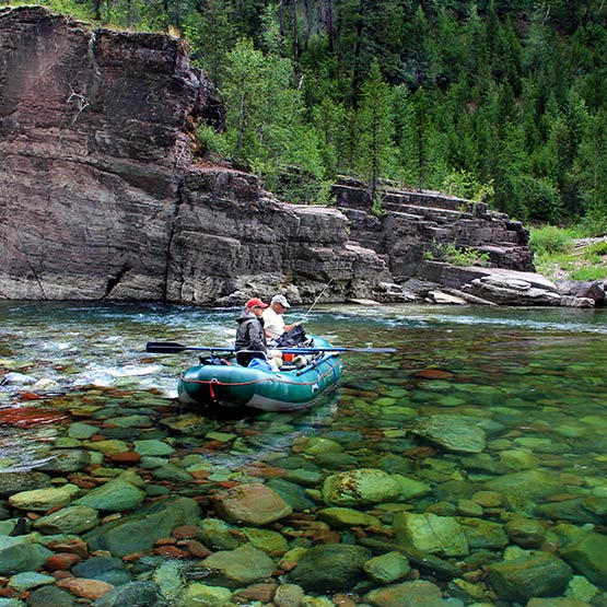 Two men float down a river with green and red rocks.