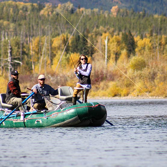 A woman reels in a fish standing on a boat.