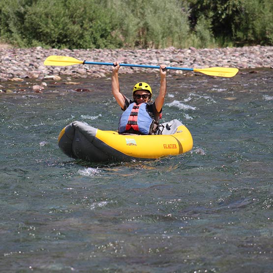 A person on a single yellow kayak lifts their paddle above their head.