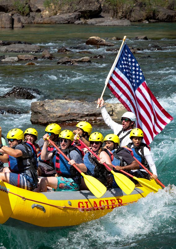 A group of rafters paddle while the guide holds a large American Flag at the back of the boat