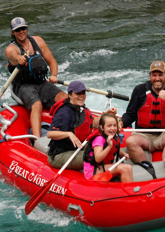 A family sits in a red raft in a rushing river.