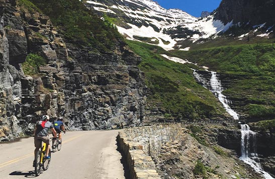 Cyclists on a narrow road next to tall cliffsides.