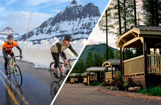 Two cyclists riding next to a snowbank. A wooden cabin under a conifer forest.