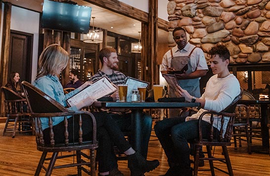 A server takes the order of 3 adults sitting at a table indoors.