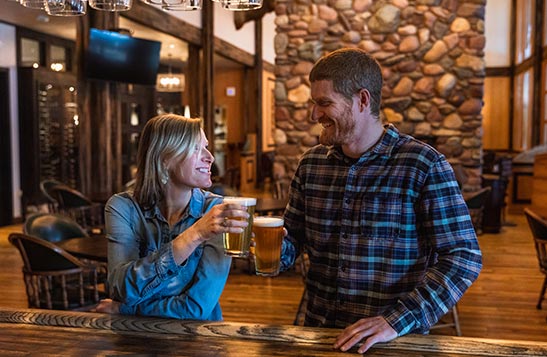 A man and woman cheer glasses of beer at a bar