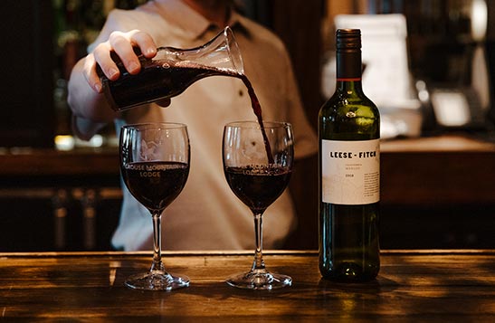 A bartender pours red wine from a container into wine glasses at a bar