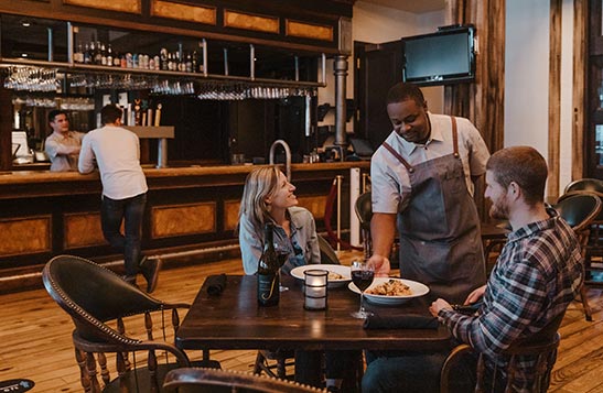 A sever puts down plates at a table with two diners