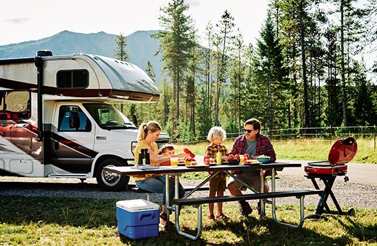 A family sitting at a picnic table outside next to their RV in spring.