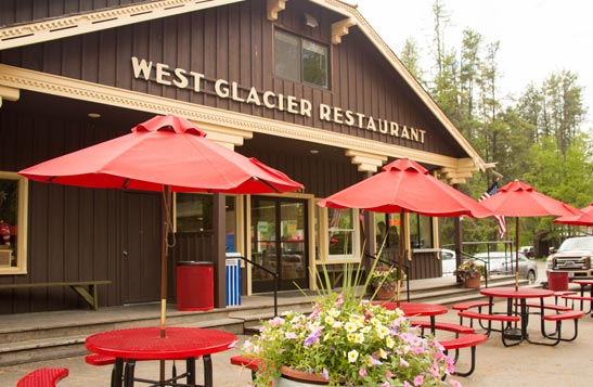 A rustic wooden building with a series of red tables out front.