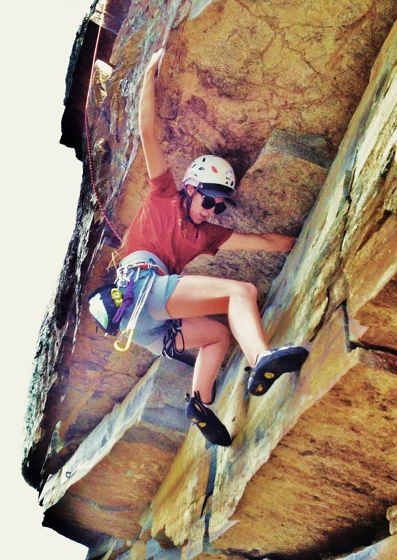 A man positions himself to climb around an overhanging cliffside