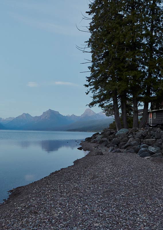 A rocky shoreline along a large calm lake with mountains rising in the distance.