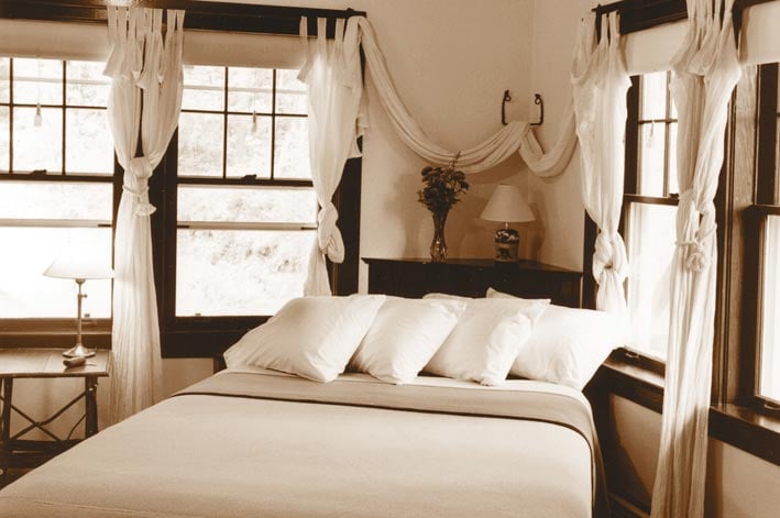 A bed in a hotel room with wide corner windows