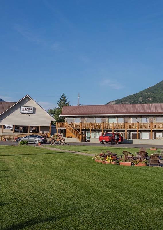 A motel building behind a green lawn below a forested mountain.