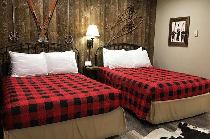 Two beds with buffalo check covers in a room with wooden walls.