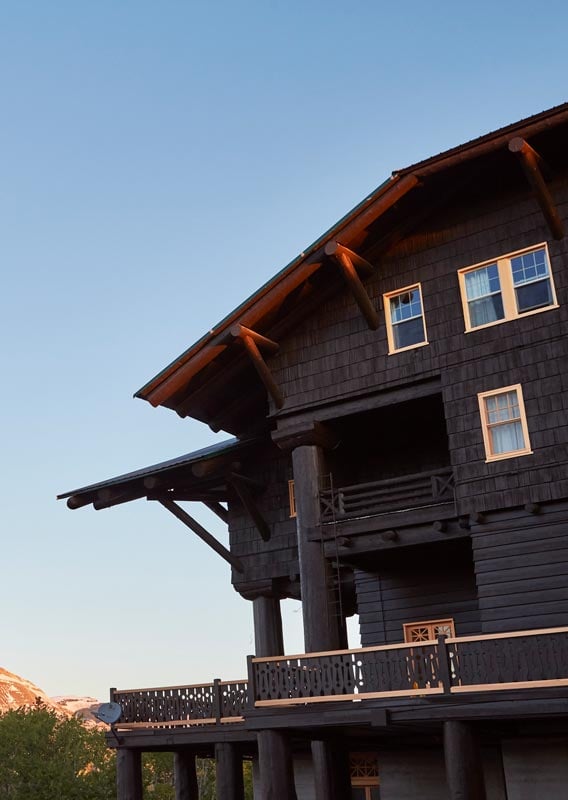 The sun shines on a mountain view behind a large wooden lodge.