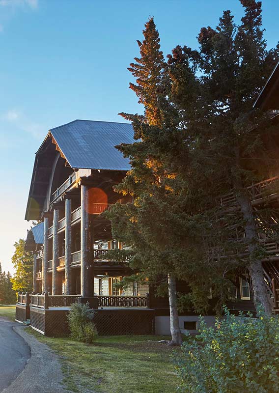 The sun shines on a grand wooden lodge, nestled among trees