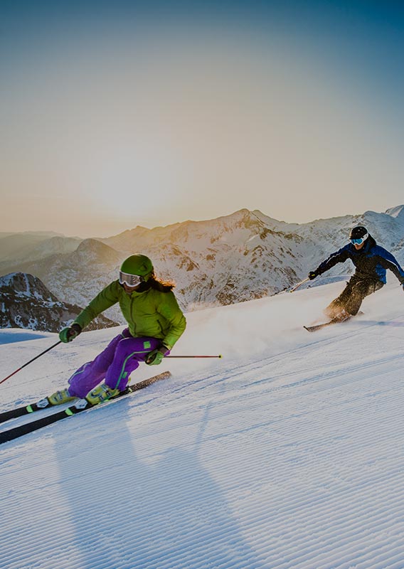 Two skiers speed down a steep slope of fresh snow.