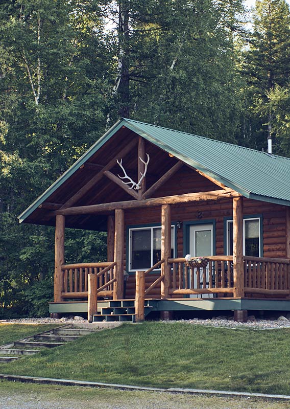 An exterior of a wooden cabin in the summer, with antlers mounted above the door.