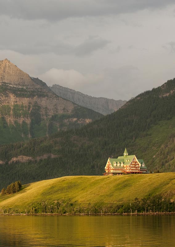 The Prince of Wales Hotel sits on a hill above a lake surrounded by mountains.