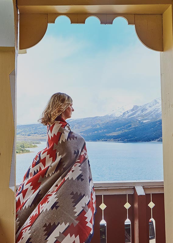 A person stands at a balcony above a blue lake.