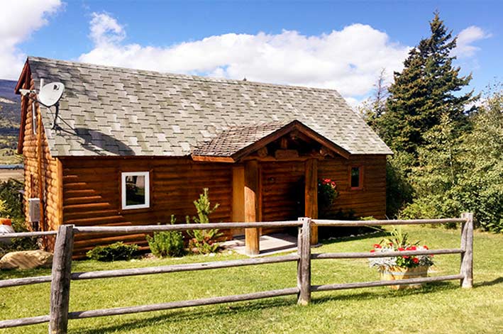 Sun Cabin at St. Mary Village, a rustic log cabin with flowers and grass in the front yard