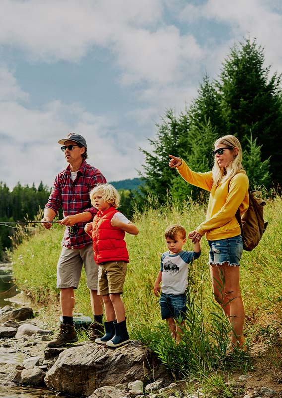 A family stands at a rivershore, with a parent holding a fishing rod.