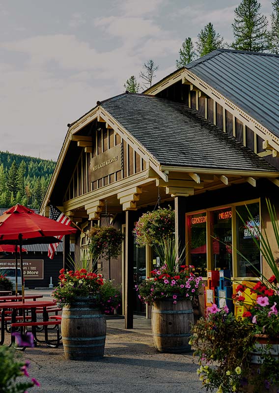 A wooden shop building with flowers in planters and patio tables.