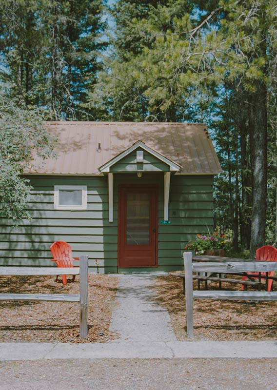 A small green cabin with red doors surrounded by trees in summer.
