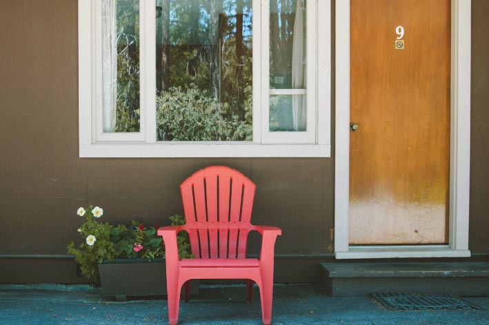 A red chair and flowerpots sits below a window next to a door.