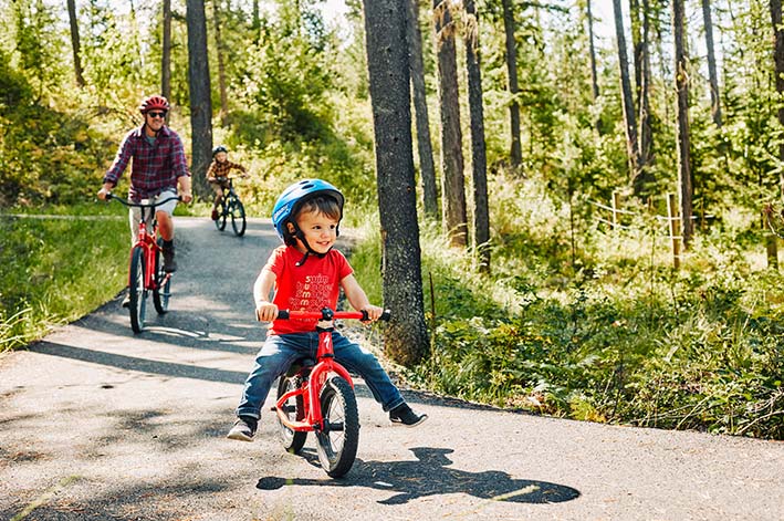 Three people ride bikes on a narrow path between trees