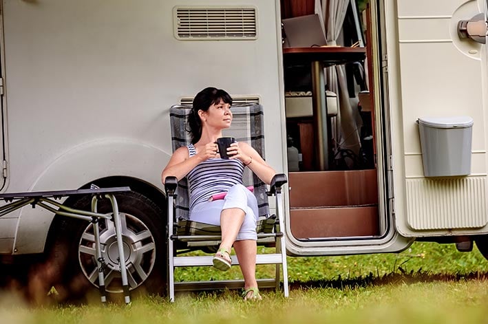 A woman sits outside an RV with a cup of coffee.