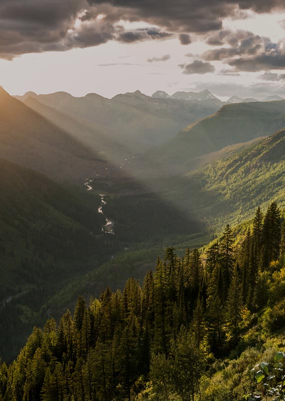 A view into a wide valley beteween tree-covered mountains.