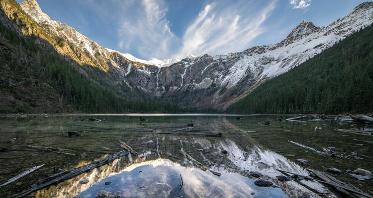 A crystal clear lake in a snowy, tree-covered alpine bowl.