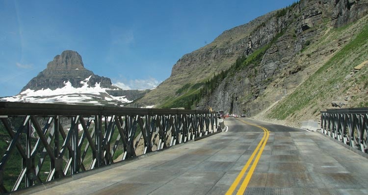 A road stretches ahead towards cliffsides and snowy mountains