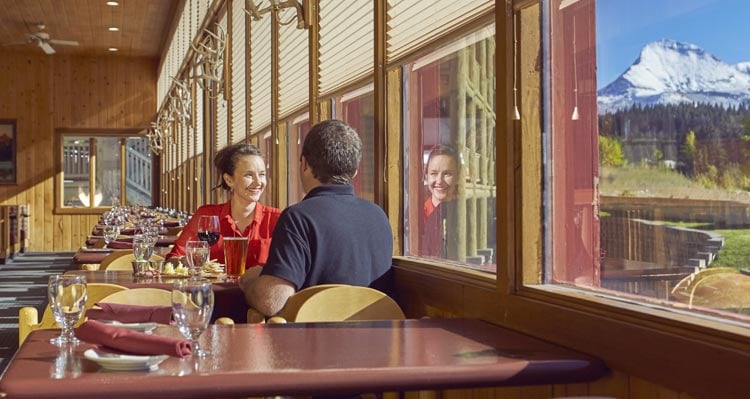 A couple sit in a restaurant dining room, looking out a window at mountain views