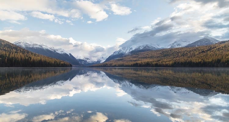 A reflecting lake between orange and green hills and snow-capped mountains.