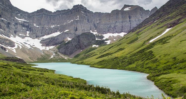 A view of a blue lake between green hills and rocky cliffs.