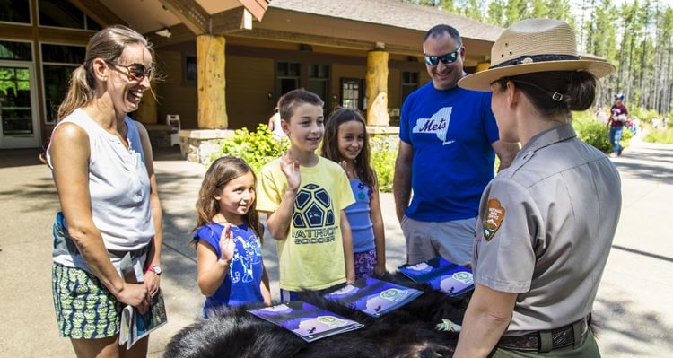A family stands with a Park Ranger in front of a wooden park information center