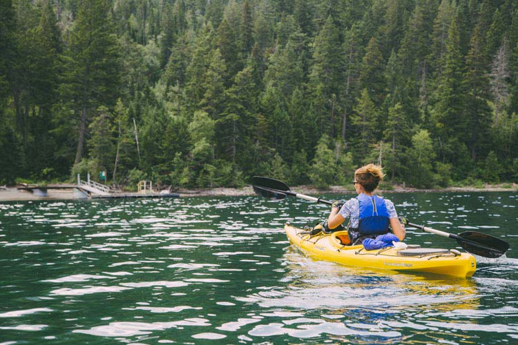 A kayaker paddles towards a dock on a forested lakeshore