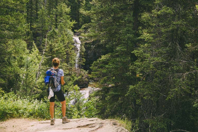 A hiker stands on a rock looking out to a waterfall and river