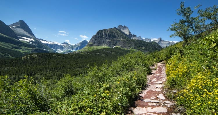 Looking down a trail towards green valleys and rocky peaks.